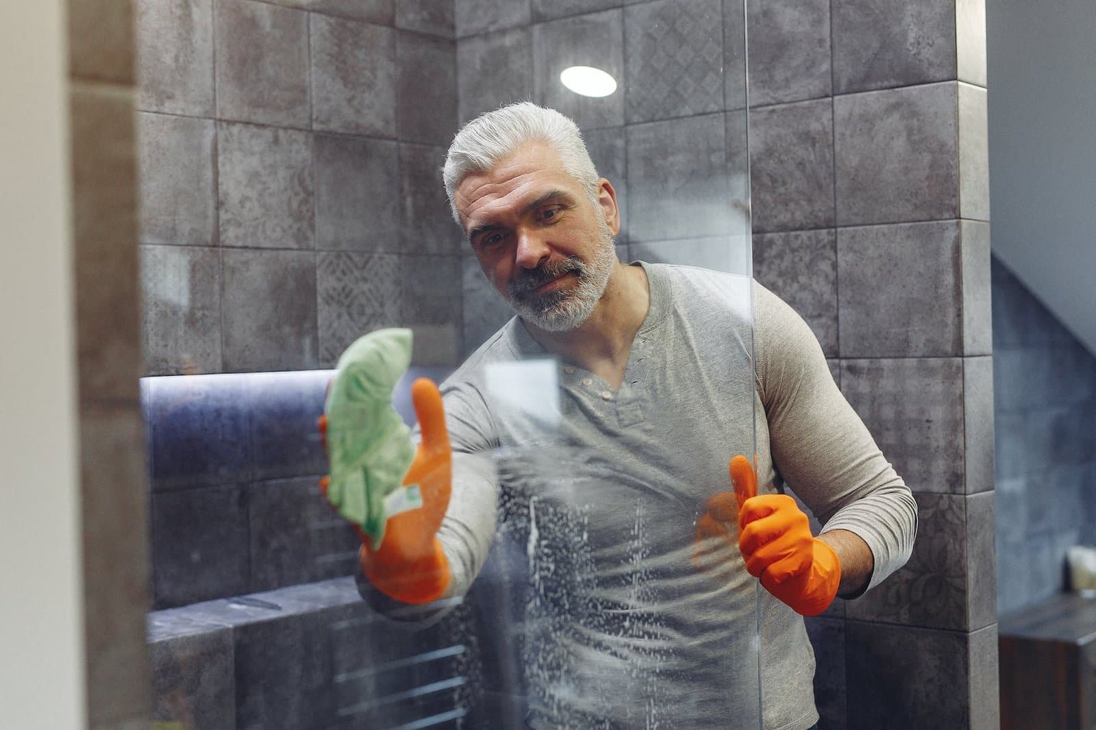 happy grey haired man wiping glass in bathroom